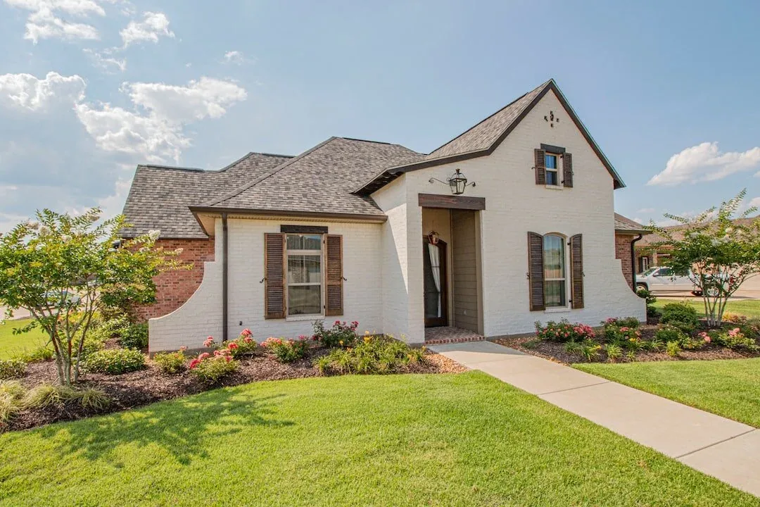 White brick cottage-style home with a manicured lawn and front walkway