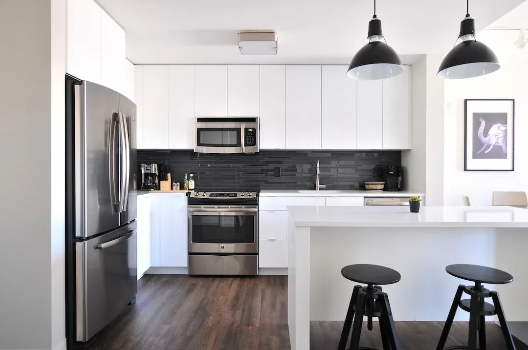White kitchen with stainless appliances, black pendant lights and an island with stools