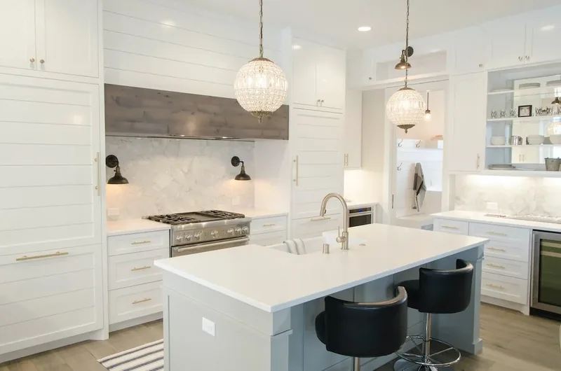 White kitchen with a marble backsplash, glass globe pendants and black counter stools